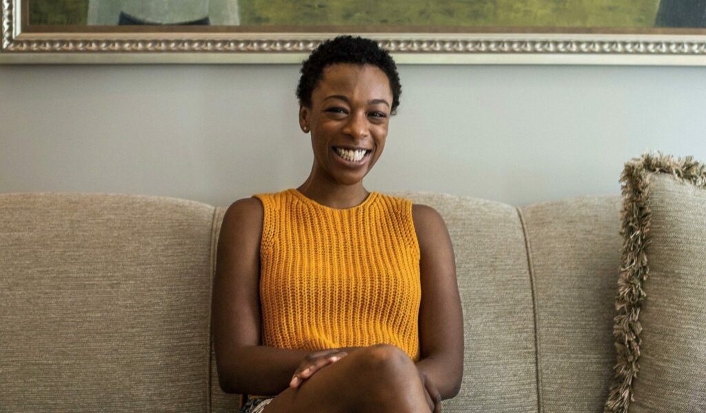 Samira Wiley in an orange top sitting on a sofa