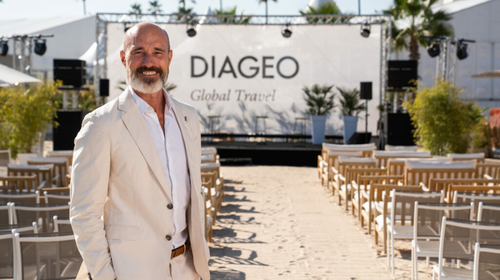 A smiling man stands in front of a DIAGEO billboard