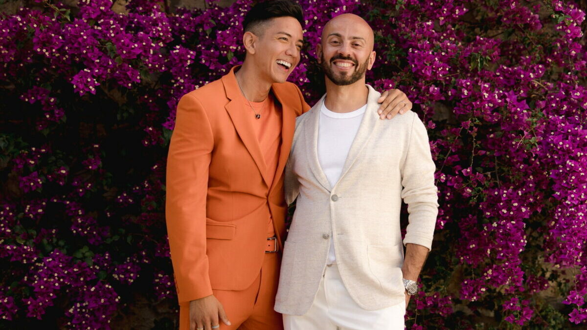 Two men embrace each other against backdrop of purple flowers