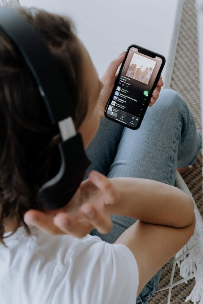 Closeup of someone holding a smartphone wearing headphones with Spotify open