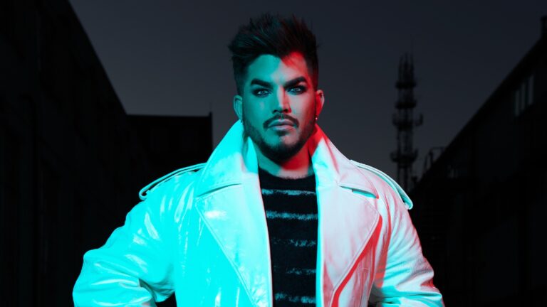 Adam Lambert stood in a dark street at night lit up in neon colours