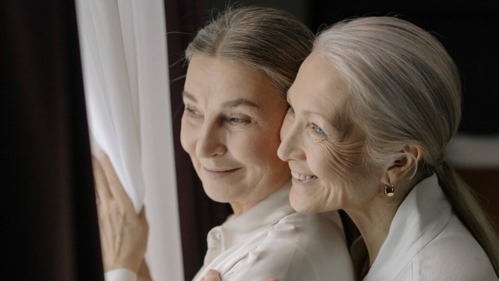 A couple of elderly women look out of their curtains of their home