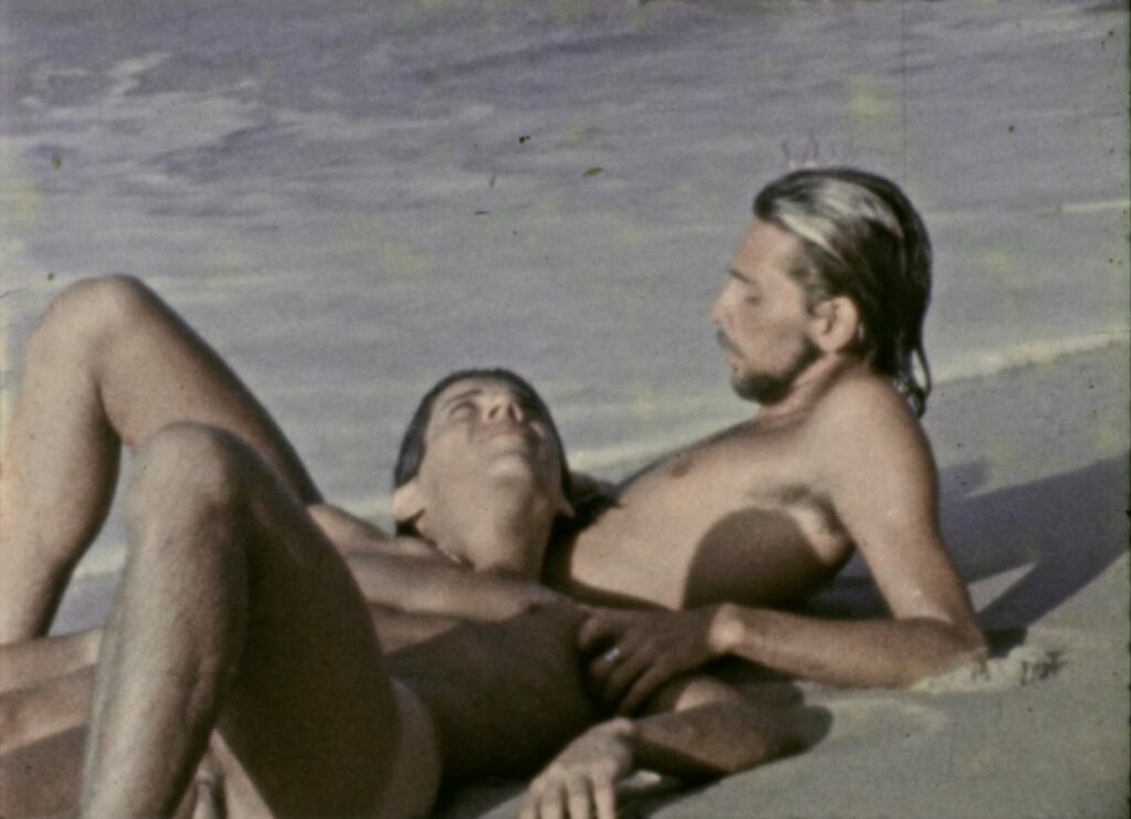 two topless men lying together on a beach
