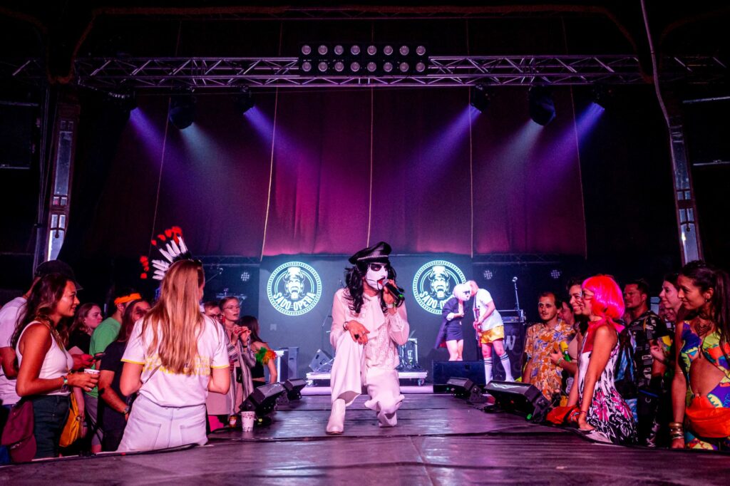 A performer on stage in a circus style tent surrounded by a crowd