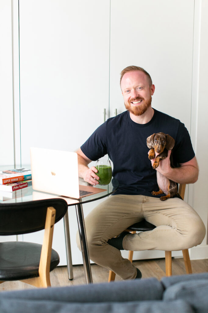 The author sitting on a stool with a green juice, holding a dog