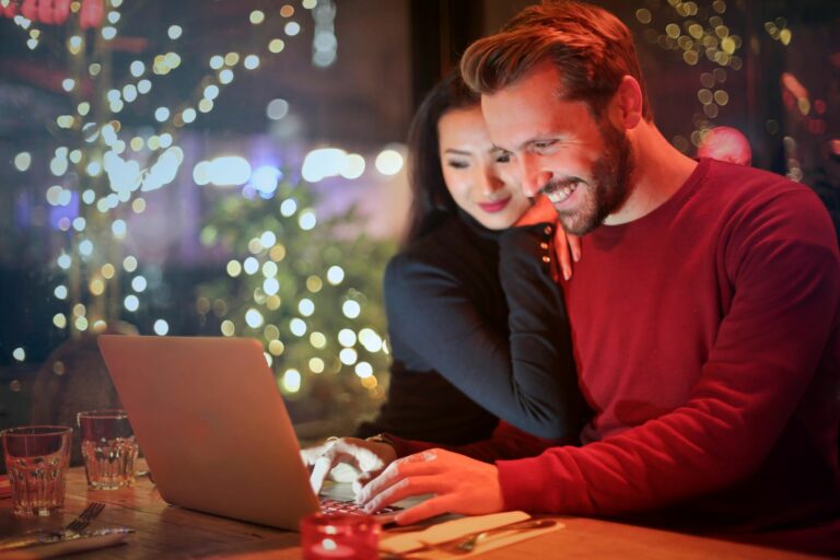 Stock image of a man in a red jumper using a laptop with a woman with a black jumper next to him
