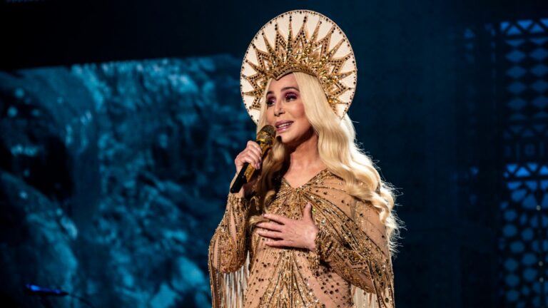 Cher performing and wearing a head dress and golden dress