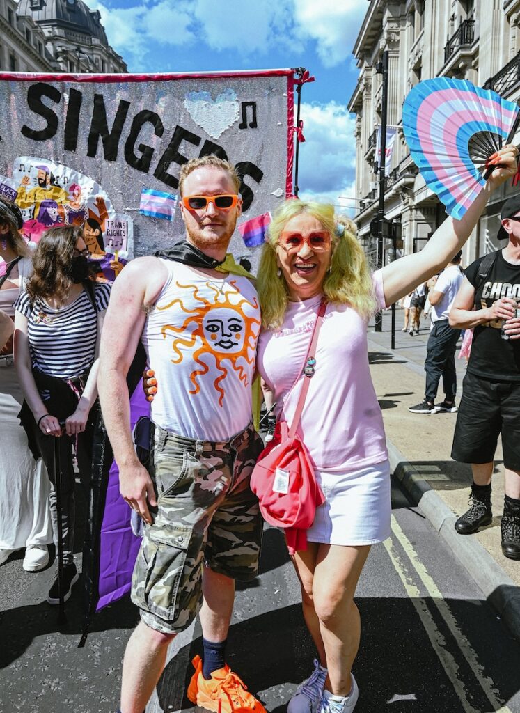 Two more Pride goers strike a pose, one with a fan in the trans flag colours