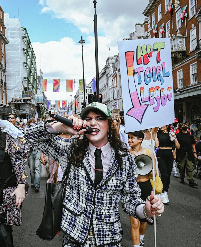 A marcher speaks into the mic while holding a sign saying 'hot t-girl lesbo'