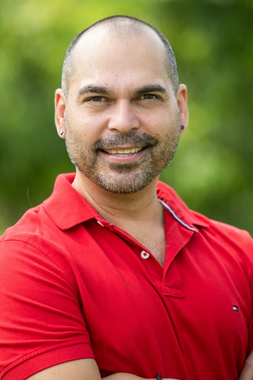 A headshot of a man wearing a red polo shirt with his arms folded