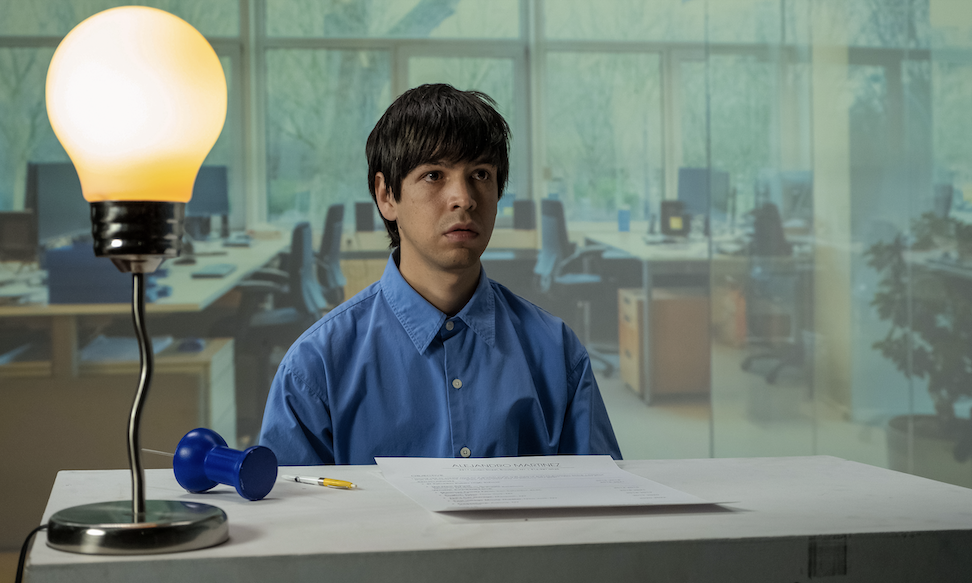 Julio Torres in character as Alejandro sitting at a desk