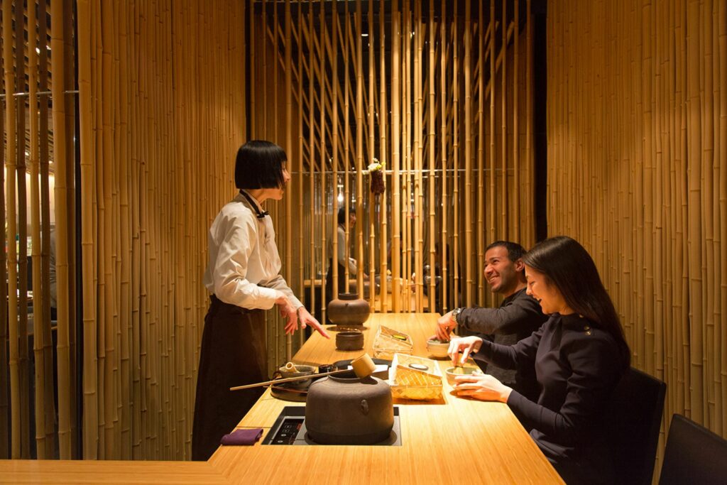 A server serves green tea to a sitting couple inside a cafe with bamboo interiror