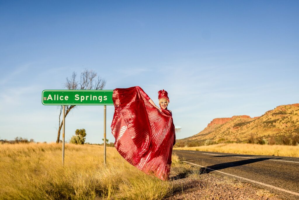 A drag queen standing in front of an Alice Springs road sign