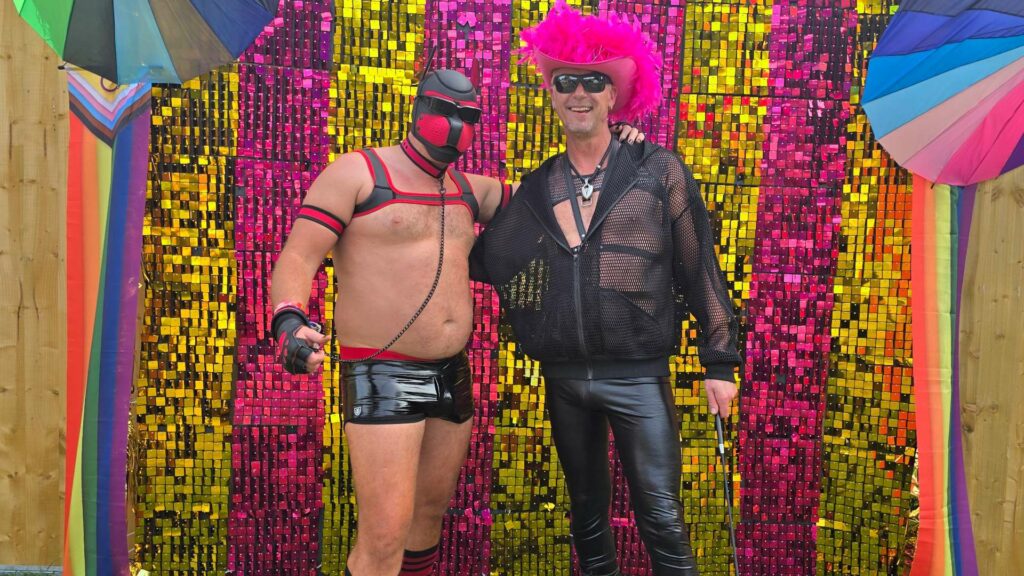 Two men in fetish outfits standing in front of a glittery backdrop