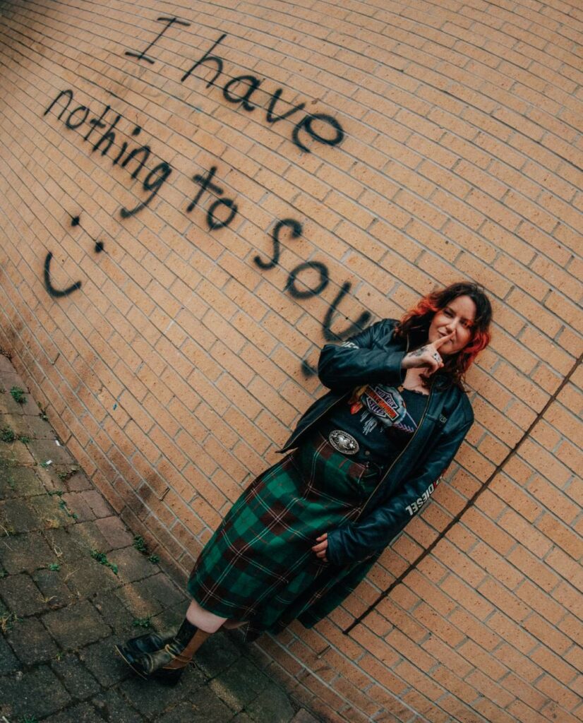 A woman standing against a wall with spray paint graffiti saying "I have nothing to say"