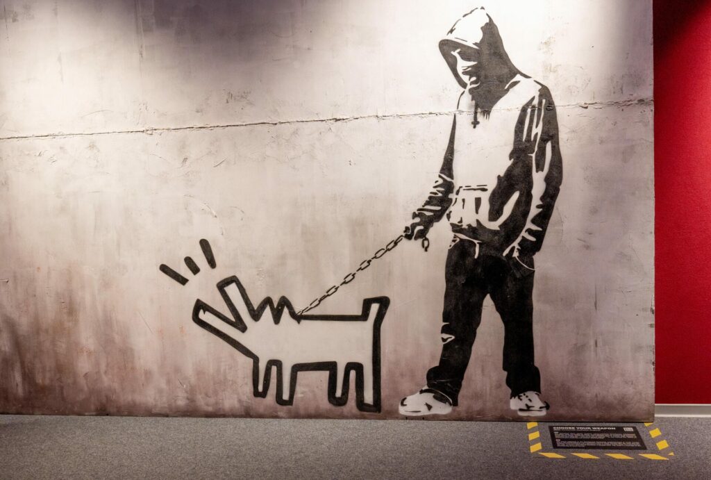 A Banksy stencil painting of a man holding a barking dog on a chain