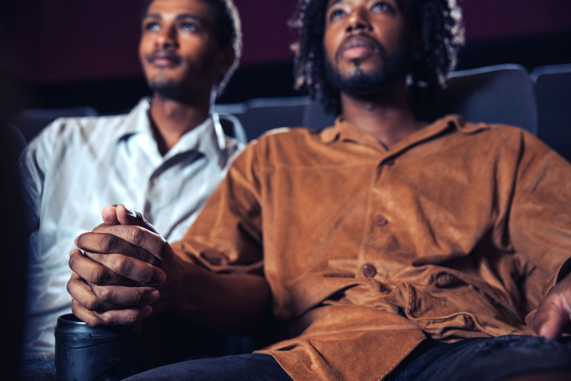 Two men holding hands in a cinema