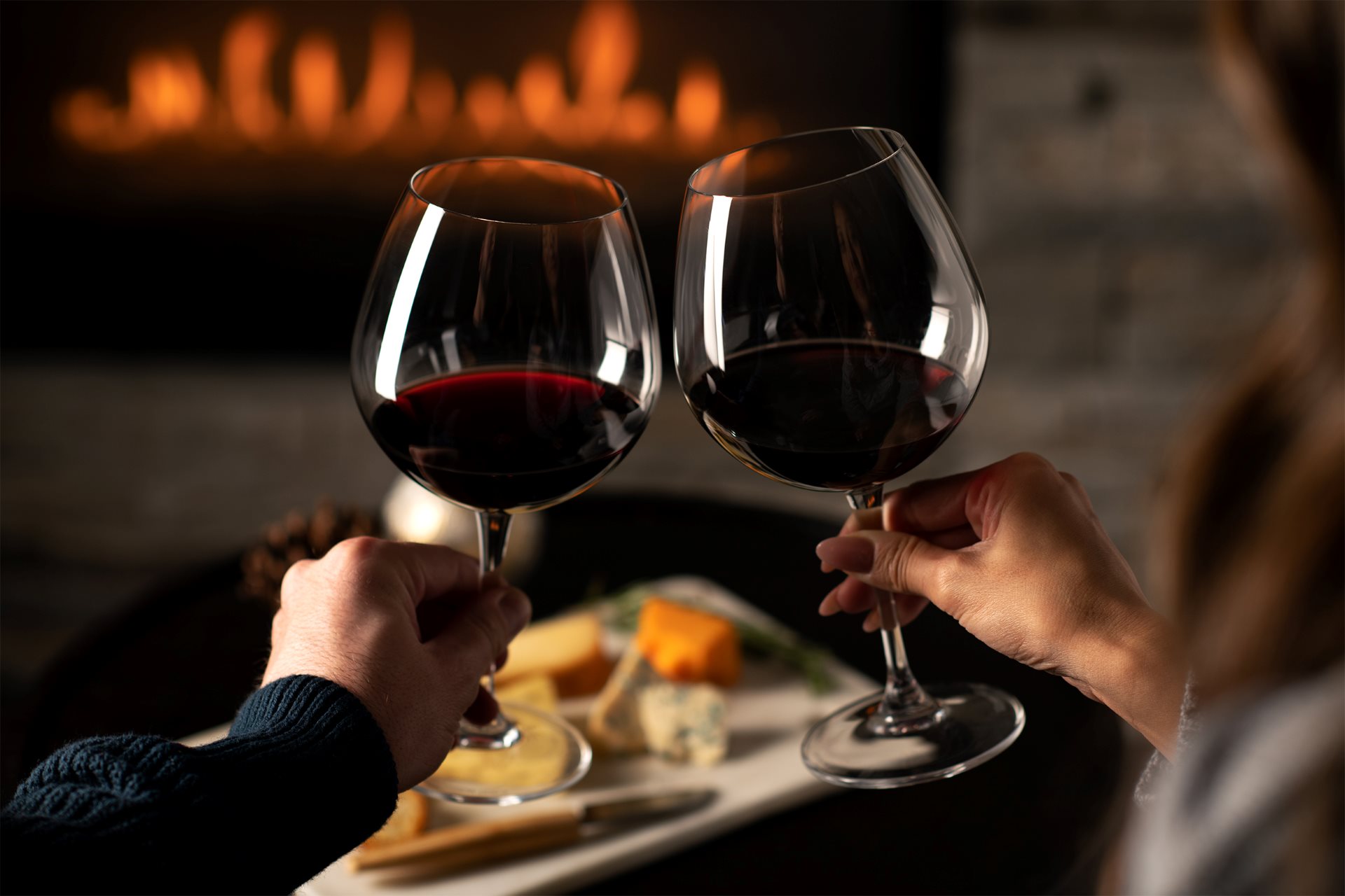 Two wine glasses clinking in front of a fireplace