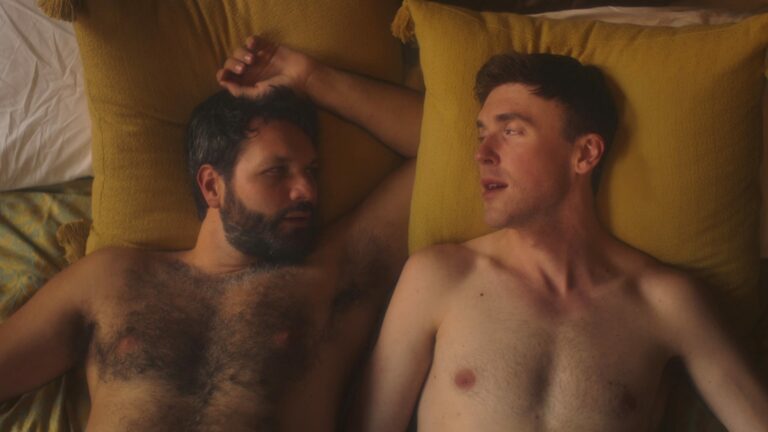 Two shirtless man lying on a bed together