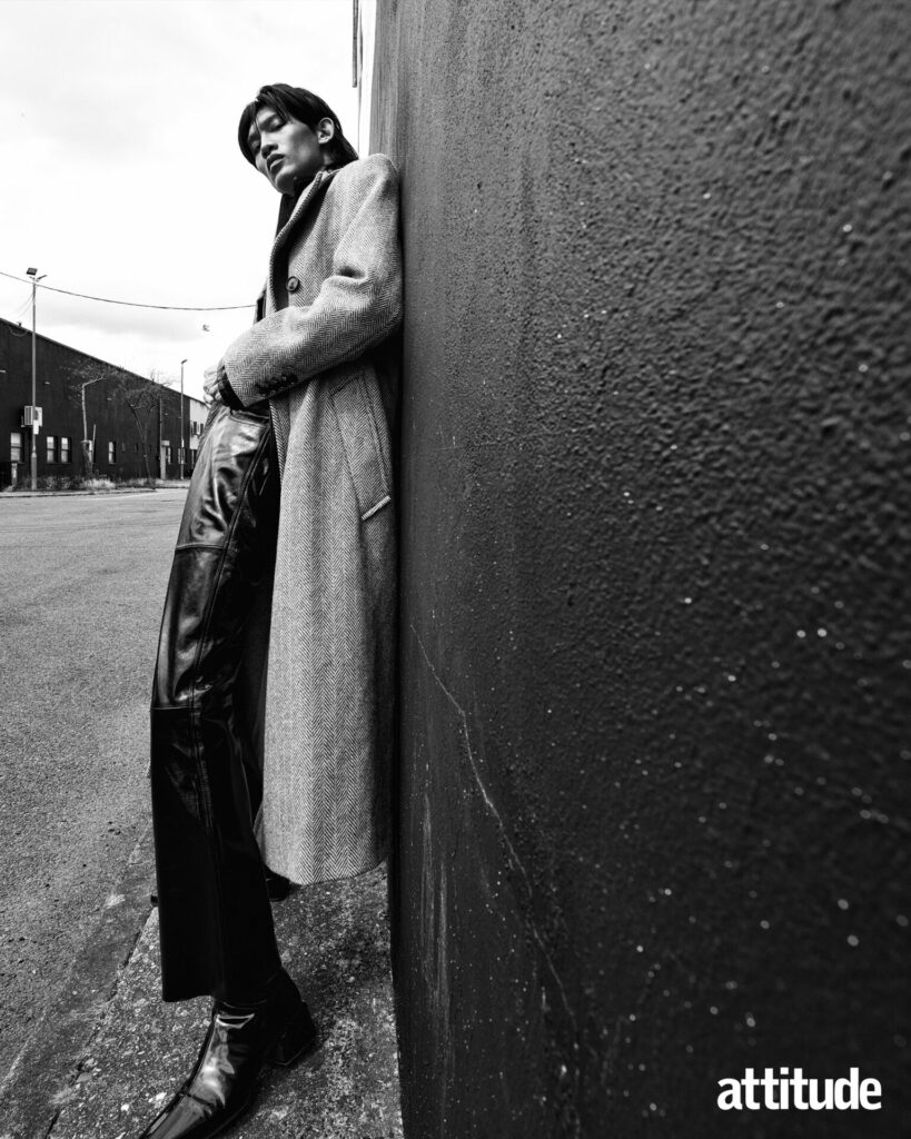 Model leans against wall in leather trousers and overcoat by AMI Paris