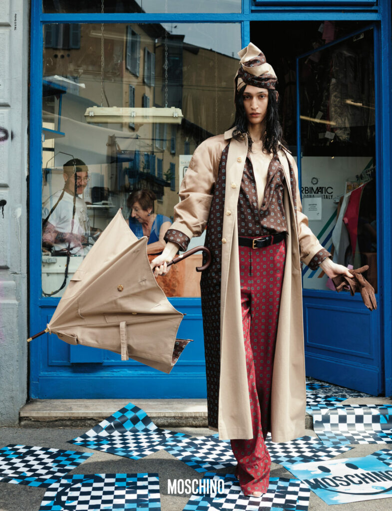 A model wearing a printed, satin shirt and trousers and beige coat holds a beige umbrella