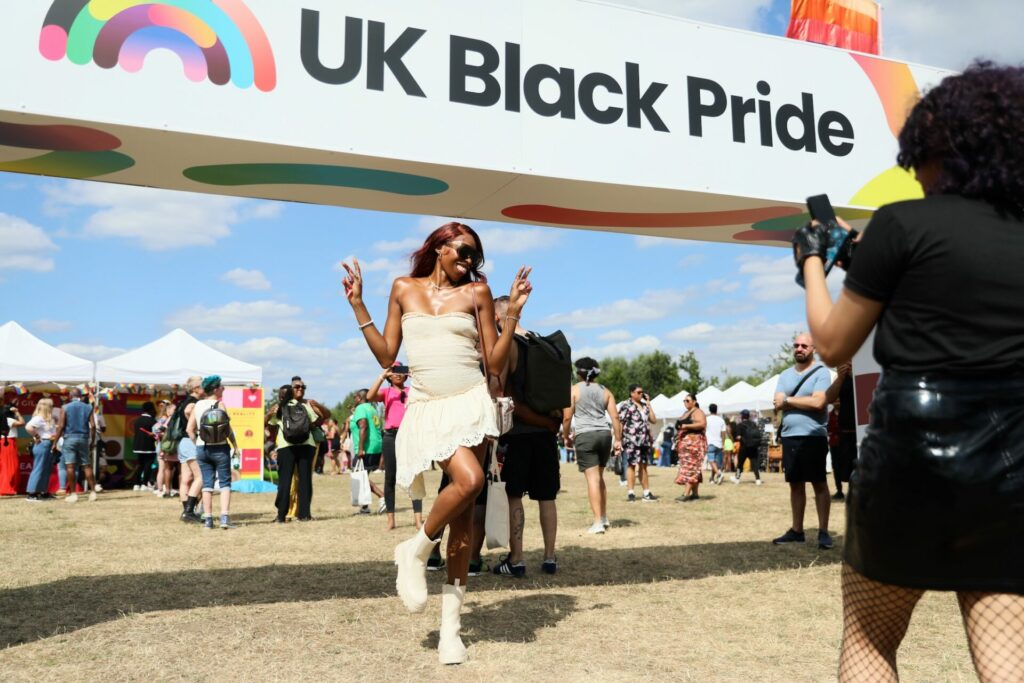 An attendee posing below the entrance which reads UK Black Pride