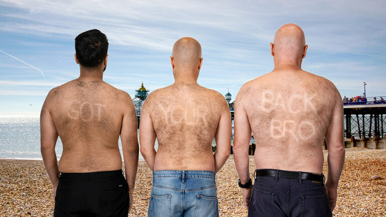 Three men at a beach with the words 'Got your back bro' on their hairy backs, spelled out by shaven areas