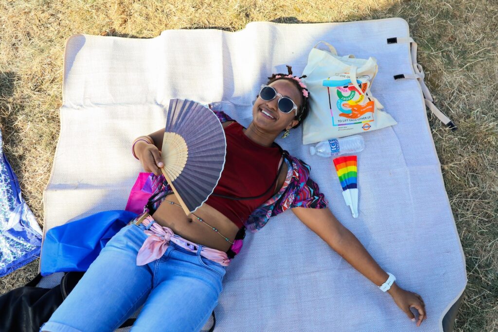 a uk black pride attendee relaxes on a throw with a fan