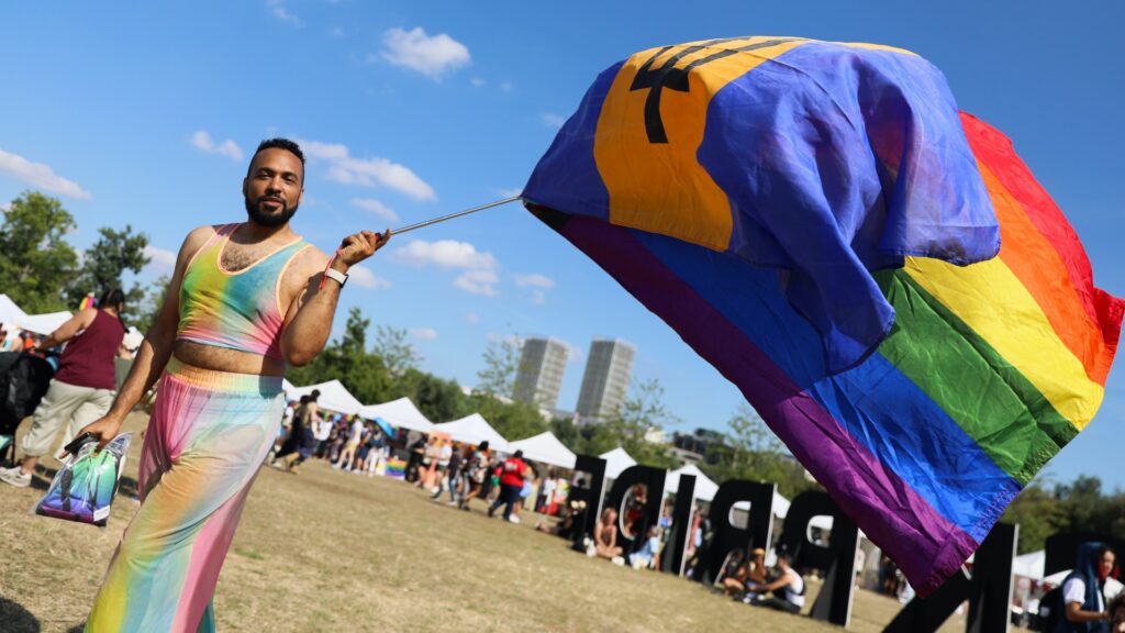 a uk black pride attendee in a rainbow dress holding a rainbow flag