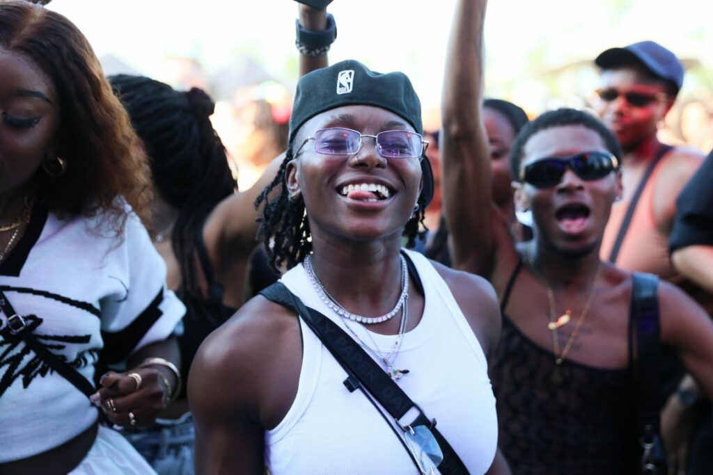 A uk black pride attendee in a white vest poses for a photo with their tongue sticking out