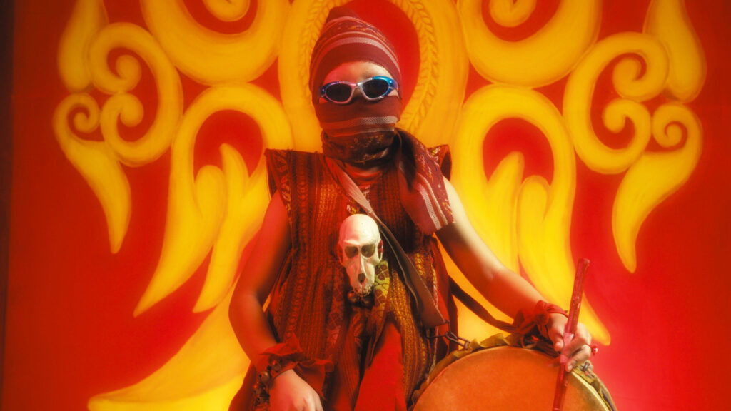 a person in a red outfit with face covered, partly by sunglasses; a still taken from one of the fringe films