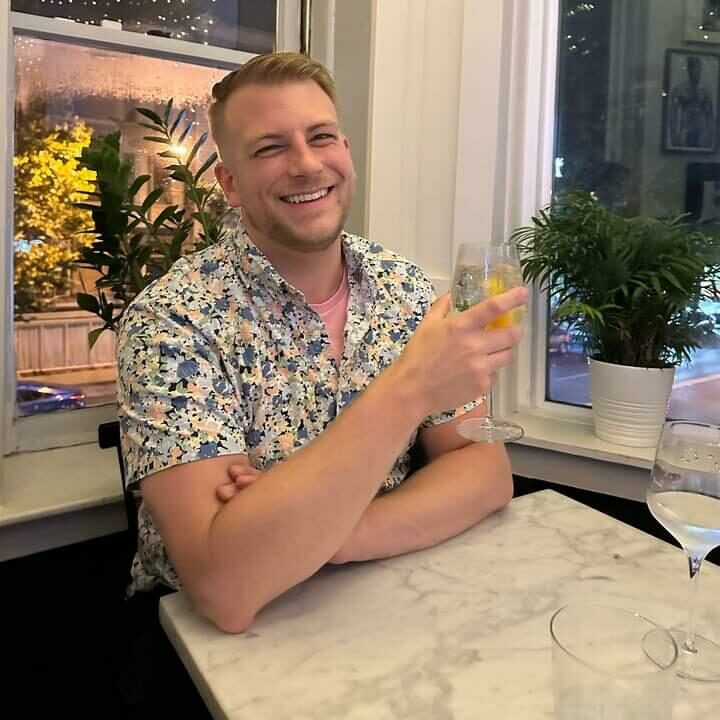 A smiling man sitting in a cafe holding a drink