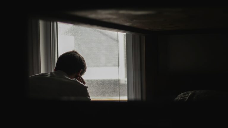 A man in shadow looking out the window