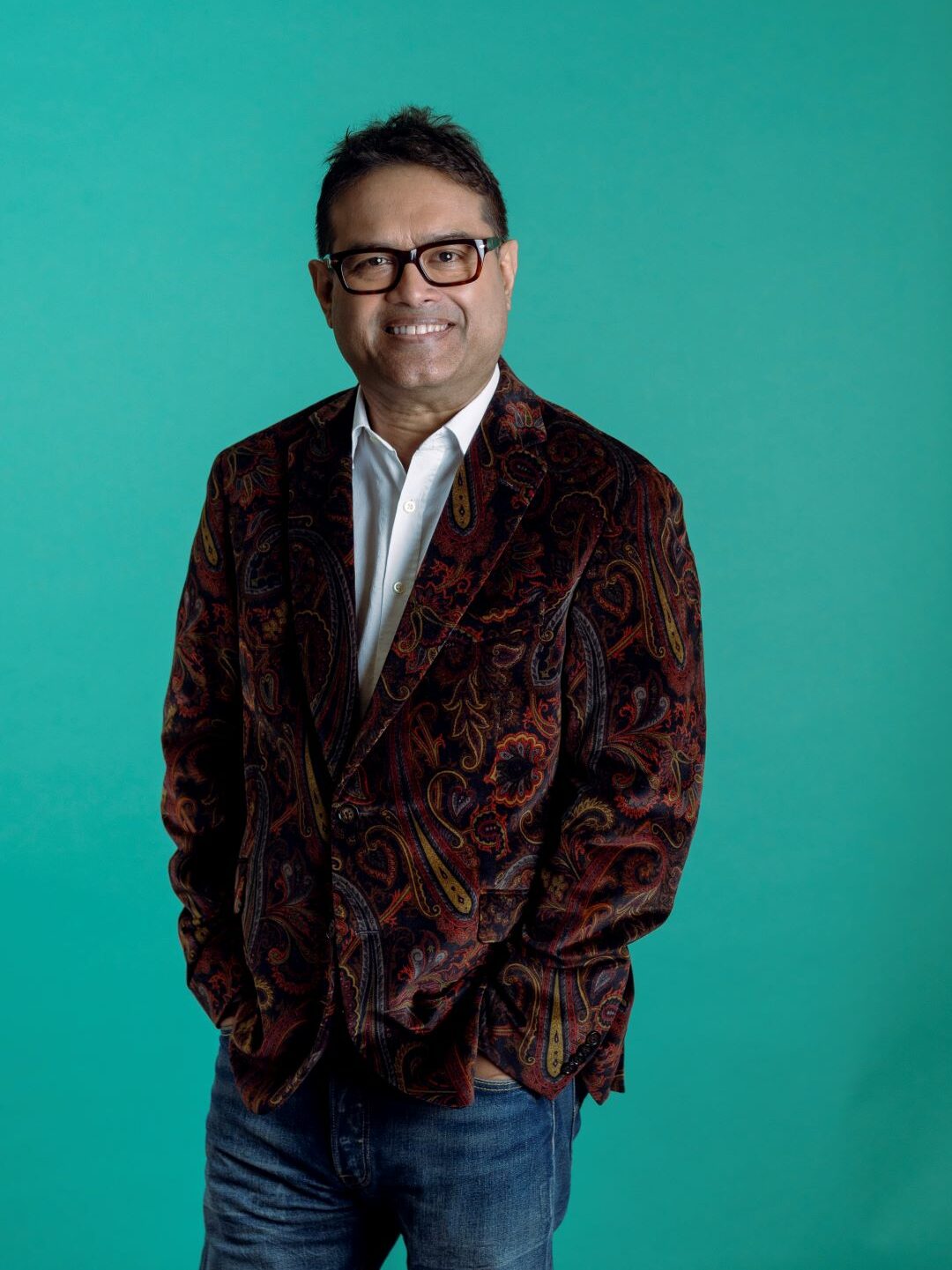 Paul Sinha standing against a green backdrop