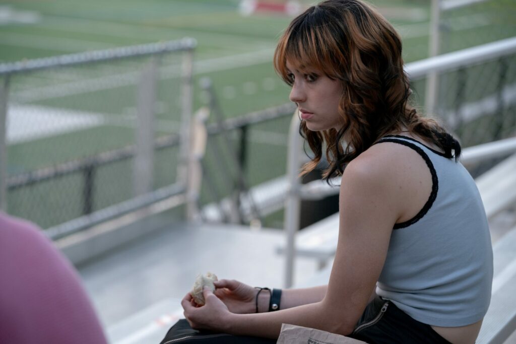 Brigette in a still from the film sitting on some bleachers in I Saw the TV Glow