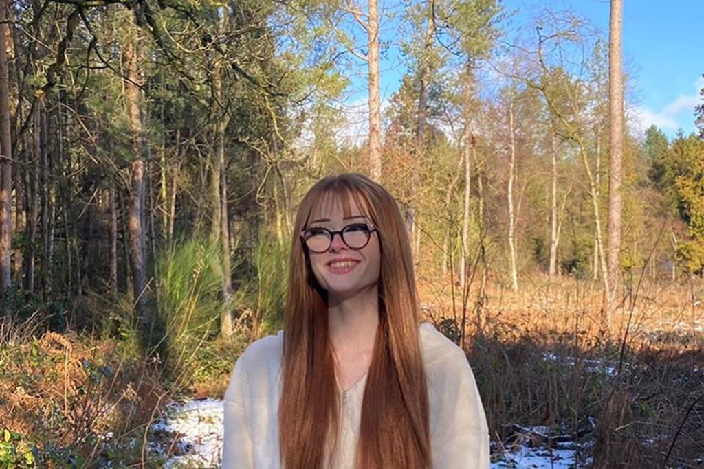 A photo of Brianna Ghey with long hair and wearing glasses, standing in front of some trees