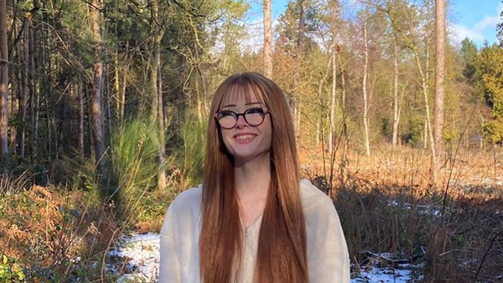 A photo of Brianna Ghey with long hair and wearing glasses, standing in front of some trees