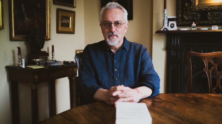 Alan Hollinghurst sitting at a table