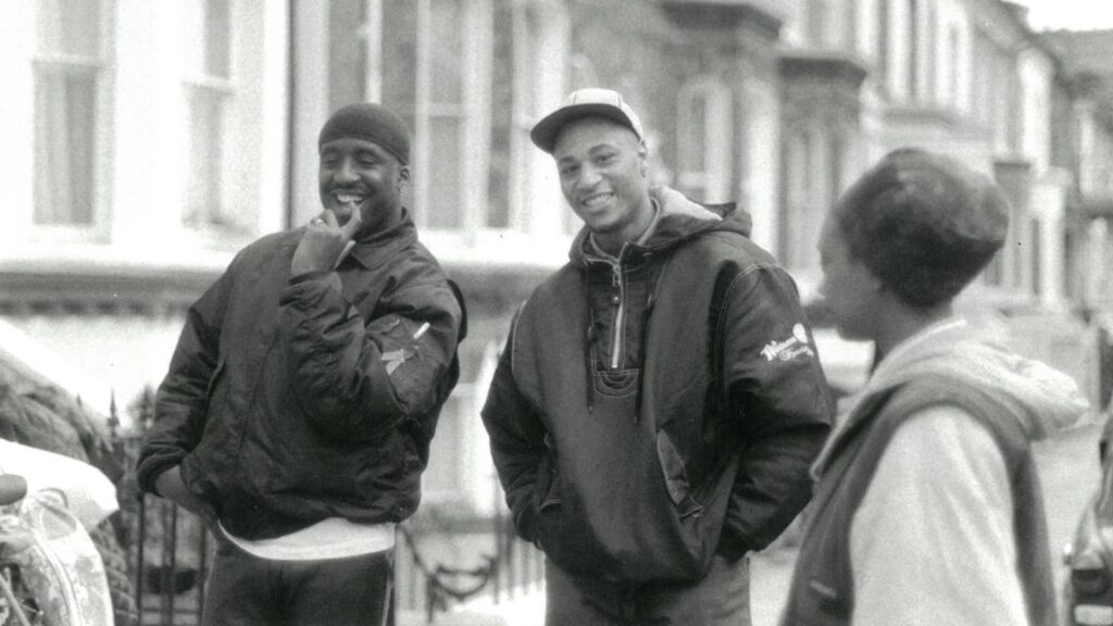 Two actors from he film in question standing on the street in black coats