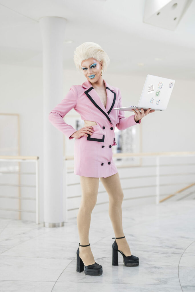 A drag queen in pink holding a laptop