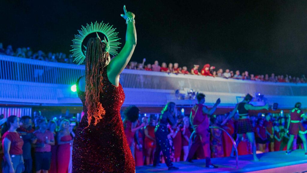 A singer performs on a Virgin Voyages ship on the deck to a crowd of people