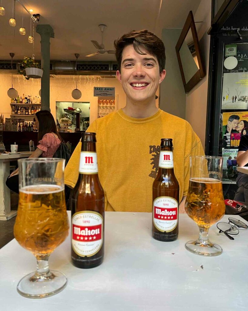 A man in a yellow jumper sitting at a table with beer bottles