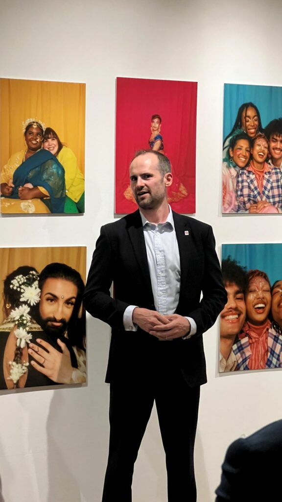 A man in a dinner jacket standing in front of a wall of paintings