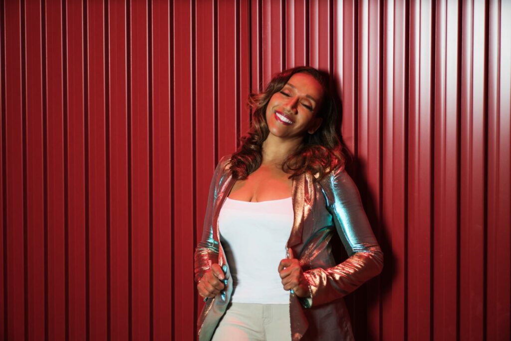 A photograph of Kathy Sledge in a shiny jacket leaning against a red wall