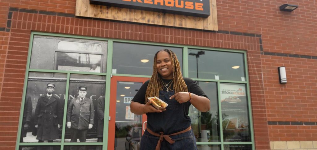 A woman stands outside a restaurant smiling