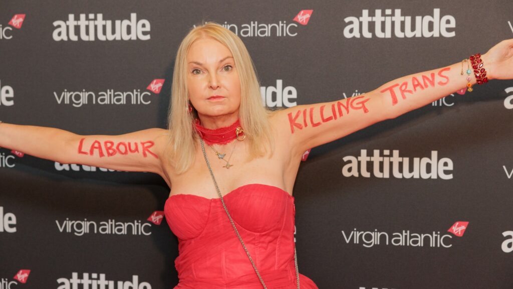 India Willoughby on the red carpet at the Attitude Awards wearing a red dress with "labour killing trans" written on her arms