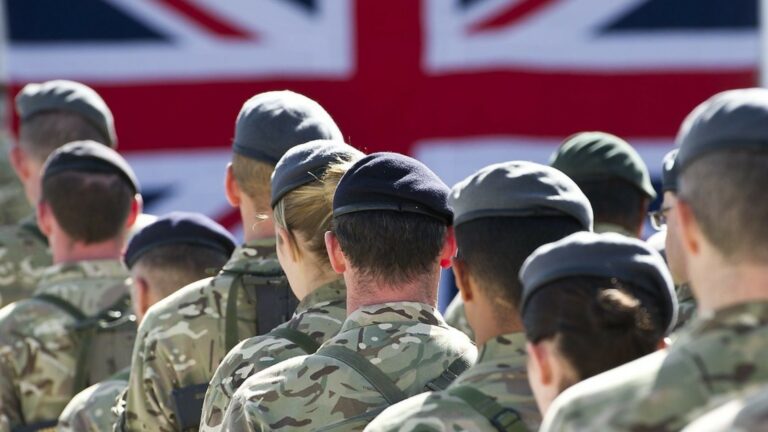 Military men and women standing in front of a Union Jack flag