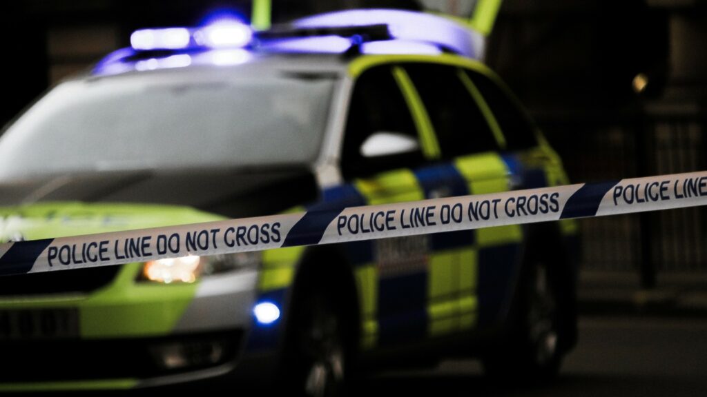 A photograph of police tape with a police car in the background