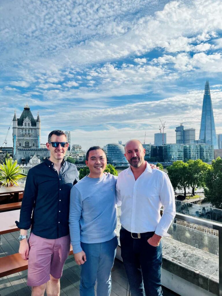 Three men standing on a rooftop with the London skyline behind them