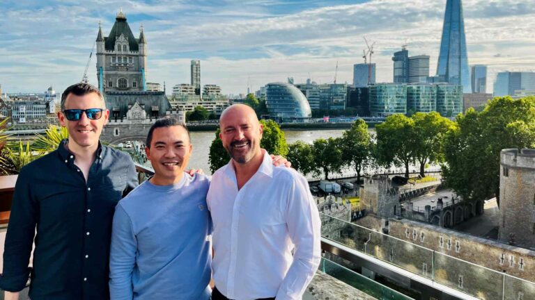 Three men standing on a rooftop with the London skyline behind them